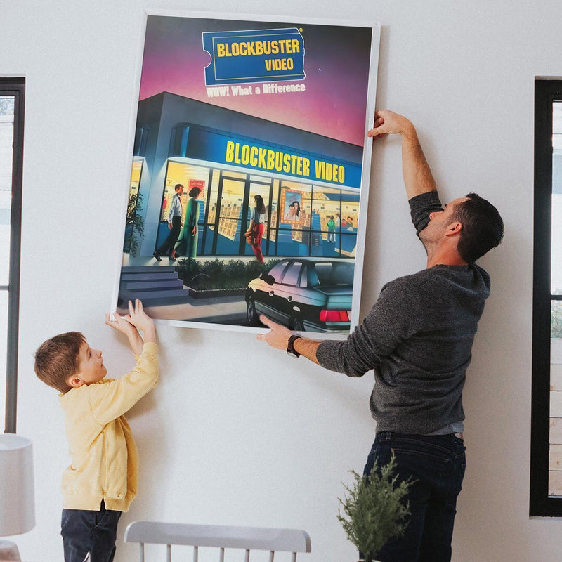 Father and son hanging the retro Blockbuster Video poster on a bright living room wall